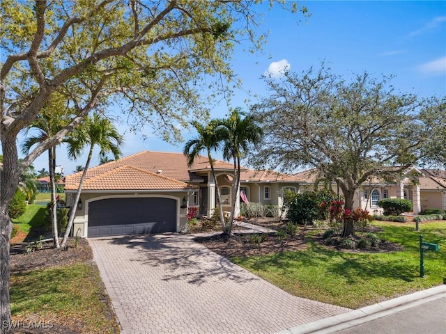 view of front of home with a garage, a tiled roof, decorative driveway, stucco siding, and a front lawn