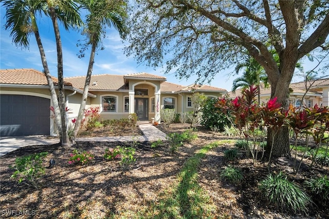 mediterranean / spanish-style house featuring a garage, a tiled roof, and stucco siding