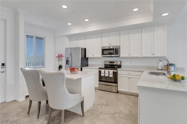 kitchen featuring stainless steel appliances, a kitchen island, a sink, white cabinetry, and ornamental molding