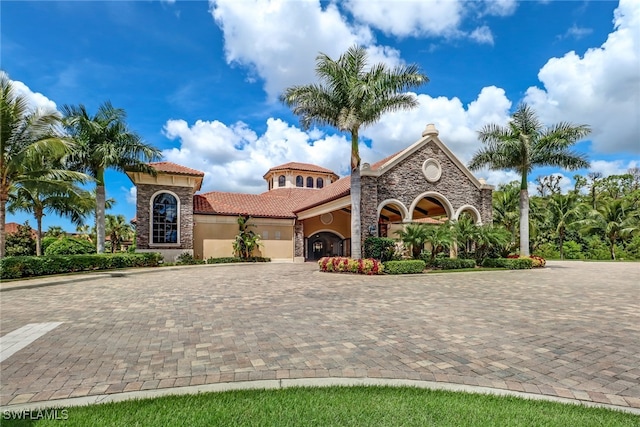 mediterranean / spanish house with stone siding, decorative driveway, a tiled roof, and stucco siding