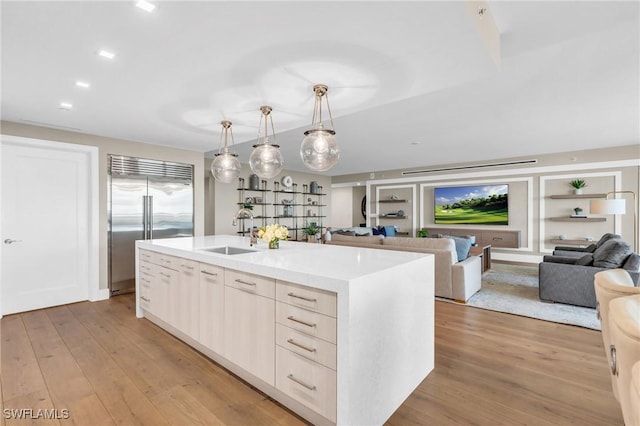 kitchen featuring stainless steel built in refrigerator, light wood-style flooring, open floor plan, and a sink