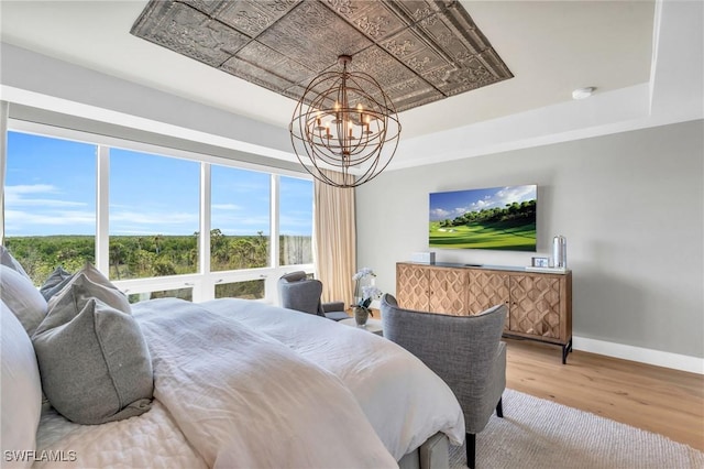 bedroom with a tray ceiling, baseboards, a chandelier, and light wood-style flooring