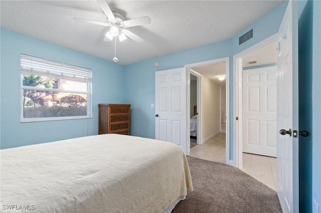 carpeted bedroom with visible vents, ceiling fan, a textured ceiling, and tile patterned floors