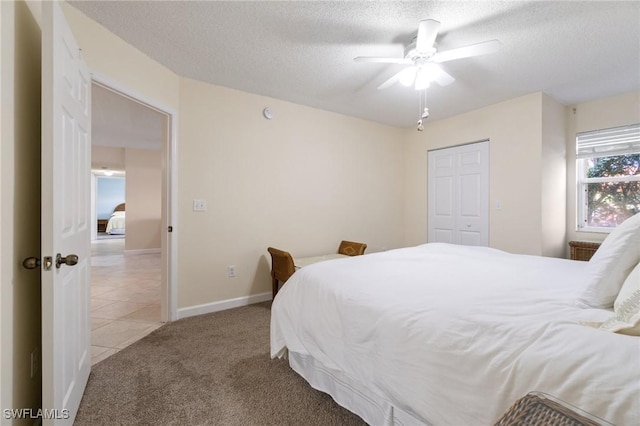 carpeted bedroom with a closet, ceiling fan, a textured ceiling, baseboards, and tile patterned floors