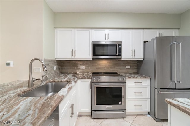 kitchen featuring light stone counters, stainless steel appliances, a sink, white cabinets, and tasteful backsplash