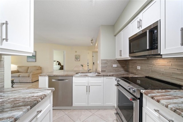 kitchen featuring stainless steel appliances, a peninsula, a sink, white cabinetry, and backsplash