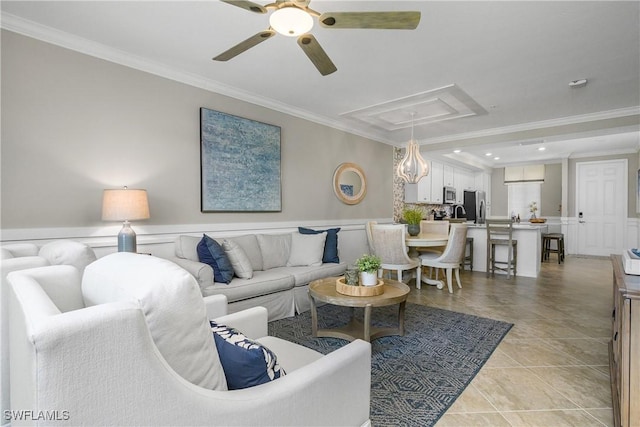 living room featuring ceiling fan, wainscoting, attic access, and crown molding