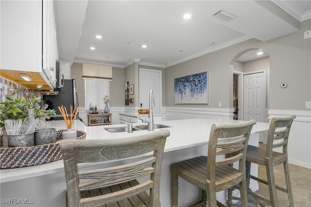 kitchen with arched walkways, a wainscoted wall, visible vents, a sink, and a kitchen bar