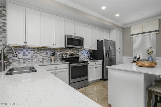 kitchen featuring white cabinets, appliances with stainless steel finishes, ornamental molding, a kitchen bar, and a sink