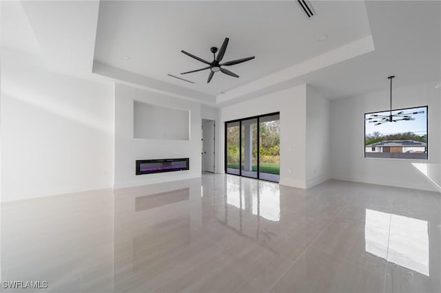 unfurnished living room with visible vents, a ceiling fan, baseboards, a tray ceiling, and a glass covered fireplace