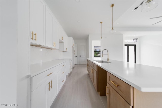 kitchen with a large island, decorative light fixtures, light countertops, white cabinetry, and a sink