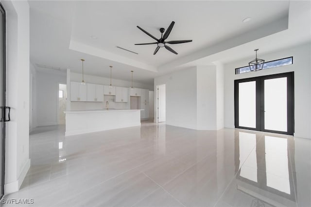 unfurnished living room with a tray ceiling, french doors, visible vents, a sink, and ceiling fan with notable chandelier