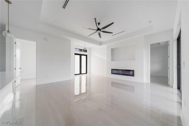 unfurnished living room with a tray ceiling, a glass covered fireplace, ceiling fan, and visible vents