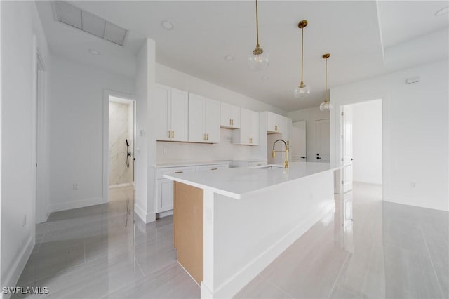 kitchen featuring a sink, white cabinetry, hanging light fixtures, light countertops, and a center island with sink