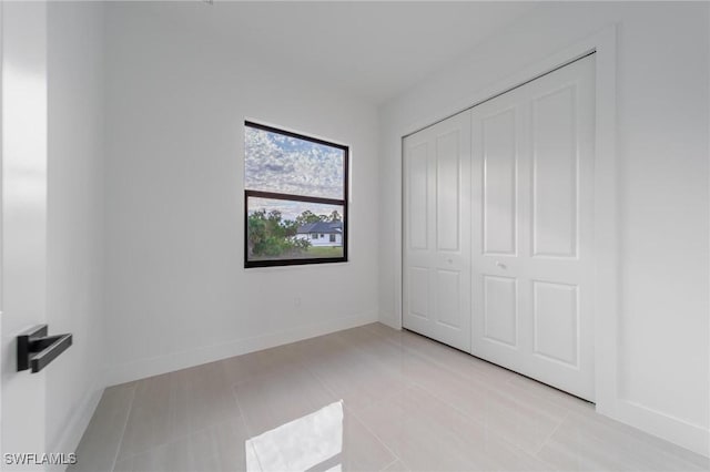 unfurnished bedroom with light tile patterned floors, a closet, and baseboards