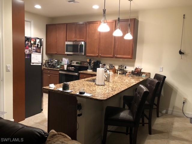 kitchen with brown cabinets, stainless steel appliances, hanging light fixtures, a peninsula, and a kitchen bar