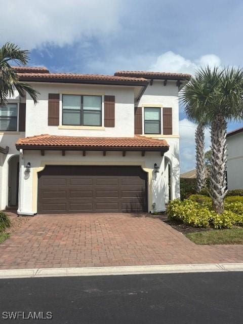 mediterranean / spanish-style house with a garage, a tile roof, decorative driveway, and stucco siding