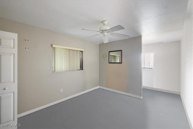 unfurnished room featuring finished concrete flooring, ceiling fan, baseboards, and a textured ceiling