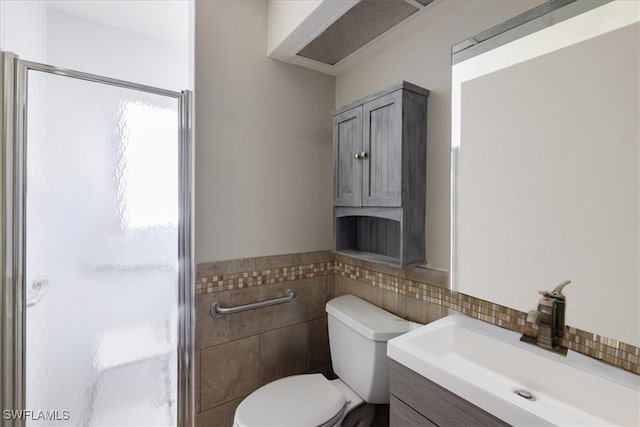 full bath featuring toilet, a wainscoted wall, vanity, tile walls, and a stall shower