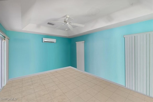 empty room featuring baseboards, visible vents, a ceiling fan, a wall unit AC, and a tray ceiling