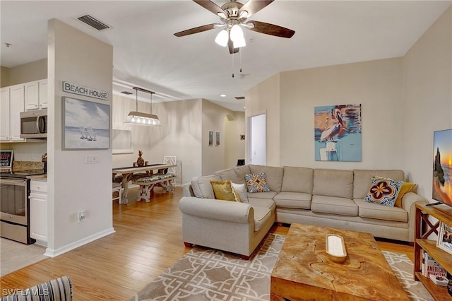 living room with a ceiling fan, light wood-type flooring, visible vents, and baseboards