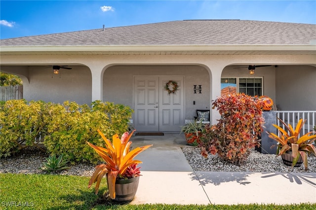 doorway to property featuring a shingled roof, a ceiling fan, a porch, and stucco siding