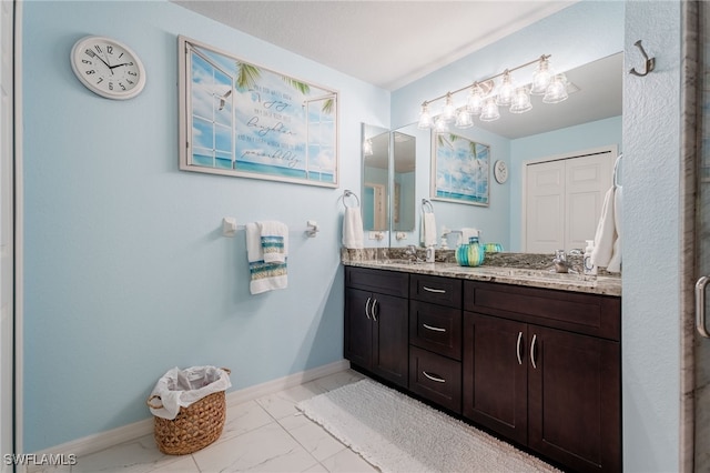 full bathroom with marble finish floor, a sink, baseboards, and double vanity