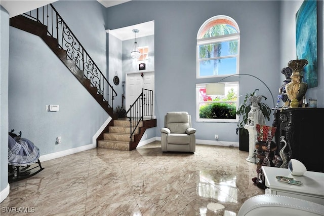 sitting room featuring a towering ceiling, marble finish floor, stairs, and baseboards