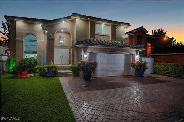 view of front of home with a tile roof, an attached garage, decorative driveway, a front lawn, and stucco siding