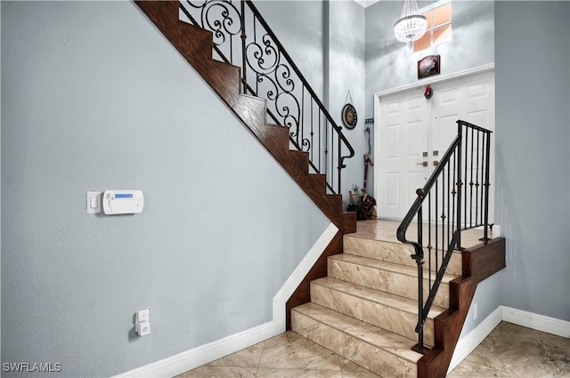 stairs featuring marble finish floor, a high ceiling, and baseboards