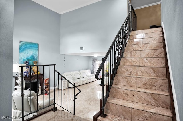 stairs featuring a towering ceiling, marble finish floor, visible vents, and crown molding