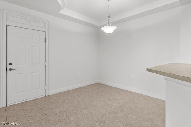 unfurnished dining area featuring a raised ceiling, light tile patterned flooring, and baseboards