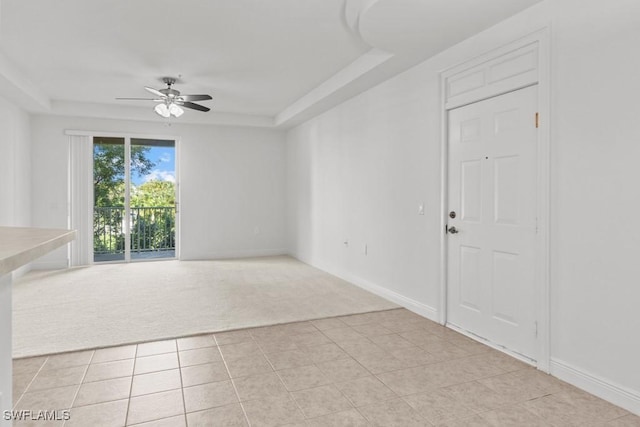 empty room with light tile patterned floors, a tray ceiling, a ceiling fan, and light colored carpet