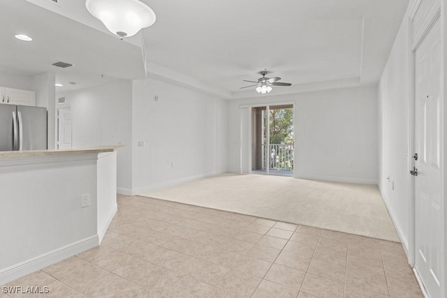 unfurnished living room with a raised ceiling, light colored carpet, visible vents, a ceiling fan, and baseboards