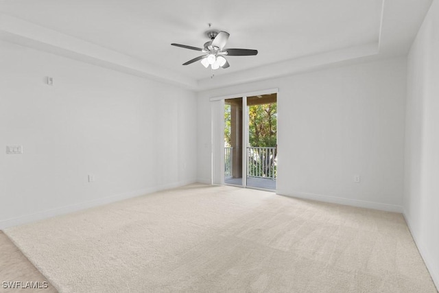 empty room with light carpet, a tray ceiling, a ceiling fan, and baseboards