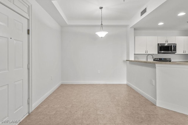 kitchen featuring light countertops, stainless steel microwave, hanging light fixtures, visible vents, and white cabinets