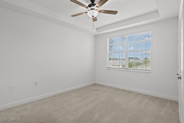 unfurnished room with a ceiling fan, a raised ceiling, light colored carpet, and baseboards