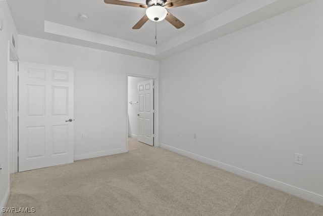 unfurnished bedroom with baseboards, a tray ceiling, and light colored carpet