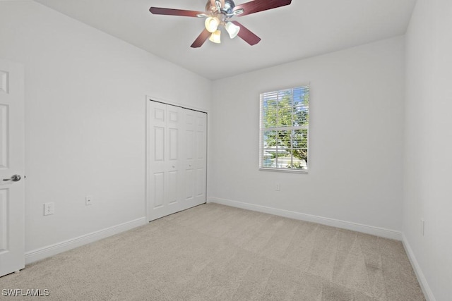 empty room featuring a ceiling fan, light colored carpet, and baseboards