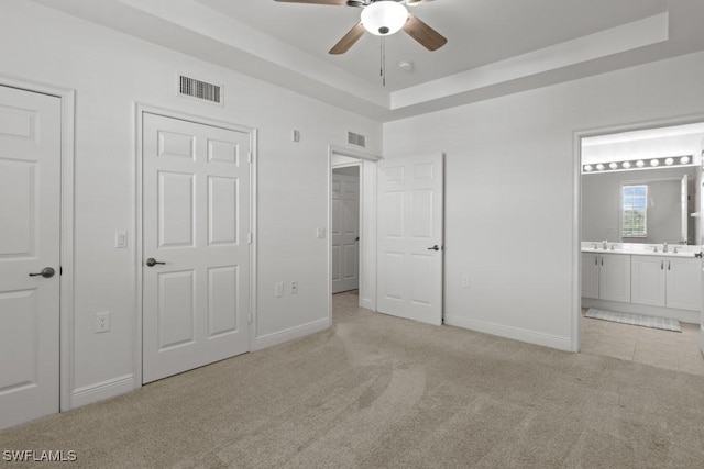 unfurnished bedroom with ensuite bathroom, a tray ceiling, visible vents, and light colored carpet