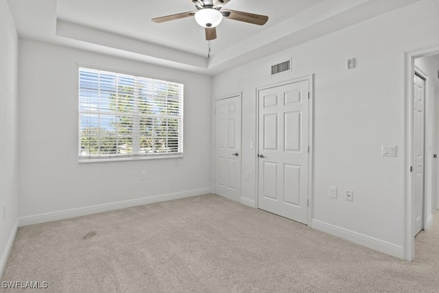 unfurnished bedroom featuring light carpet, a raised ceiling, visible vents, and baseboards