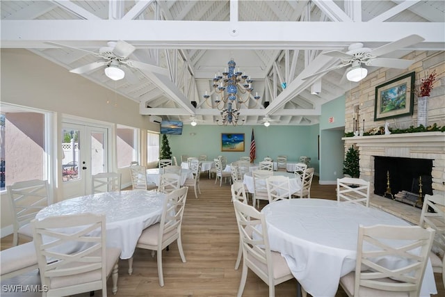 dining area with ceiling fan with notable chandelier, french doors, a fireplace, and wood finished floors