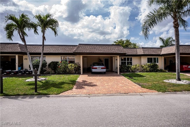 single story home featuring decorative driveway, mansard roof, an attached carport, and a front yard