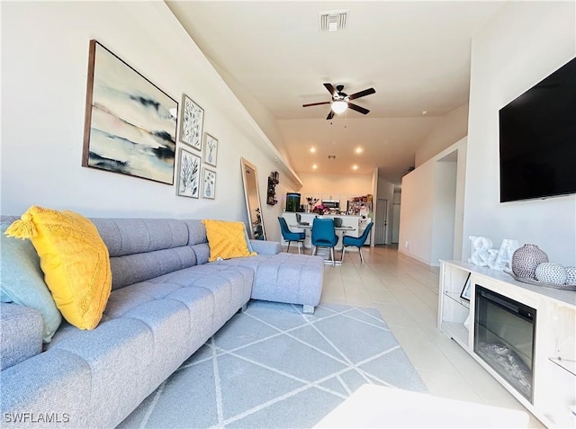 living area featuring light tile patterned floors, visible vents, a glass covered fireplace, lofted ceiling, and ceiling fan