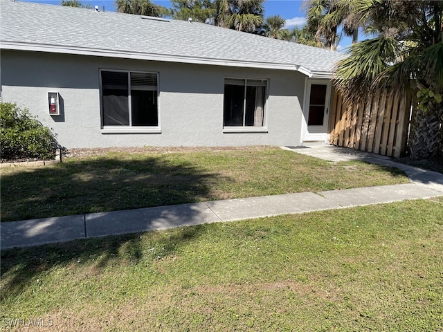 exterior space featuring a front yard, roof with shingles, fence, and stucco siding