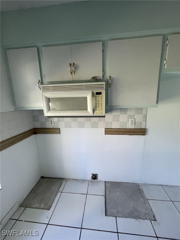 kitchen featuring white microwave, light tile patterned floors, and backsplash