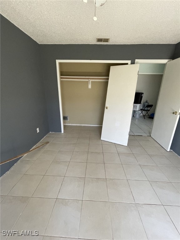 unfurnished bedroom with a textured ceiling, a closet, light tile patterned flooring, and visible vents