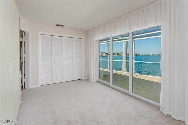 unfurnished bedroom featuring a water view, visible vents, access to exterior, a closet, and carpet