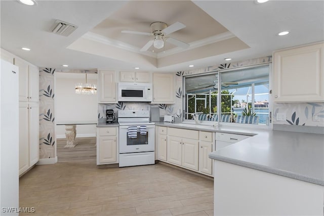 kitchen with white appliances, visible vents, a raised ceiling, and a sink