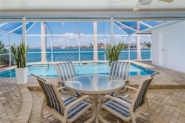 pool with ceiling fan, glass enclosure, a patio, and a water view